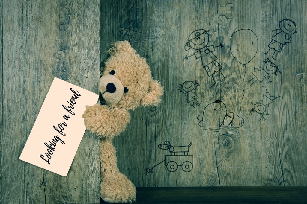 Ein Teddy, der hinter einer Tür hervor schaut und einen Zettel mit der Aufschrift: "Looking for an friend" in der Hand hält