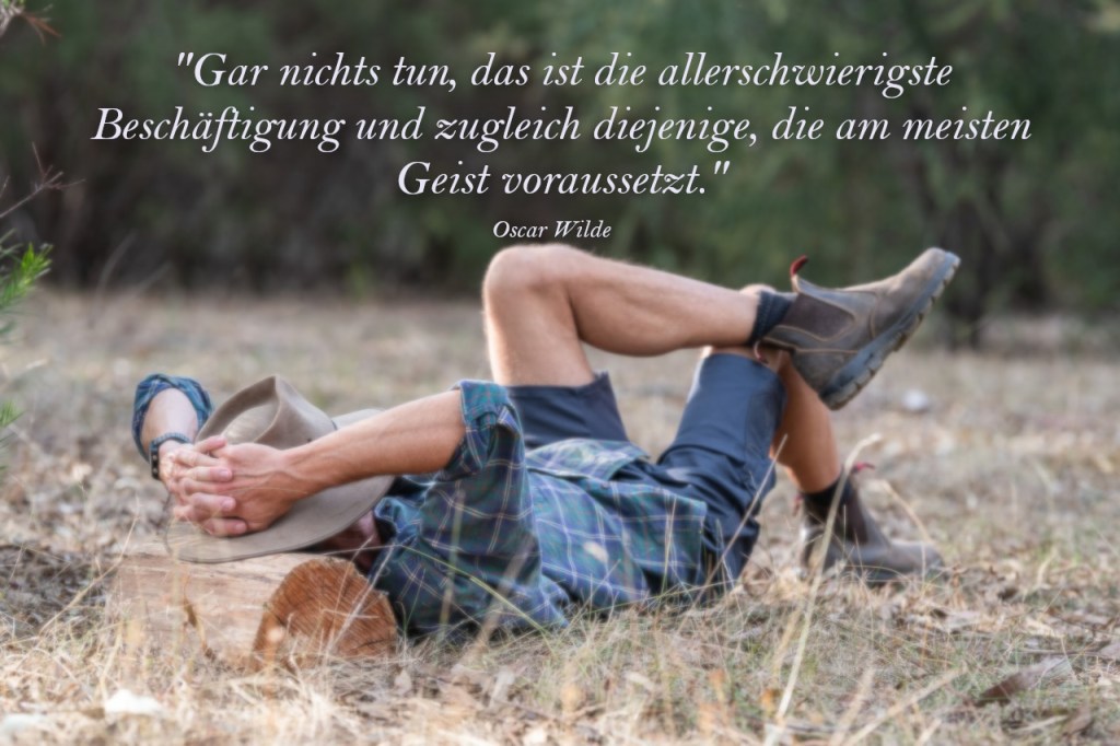 Ein Mann liegt auf einer Wiese. Die Hände hat der hinter dem Kopf geschlagen. Sein Kopf liegt auf einem Stück Holz.