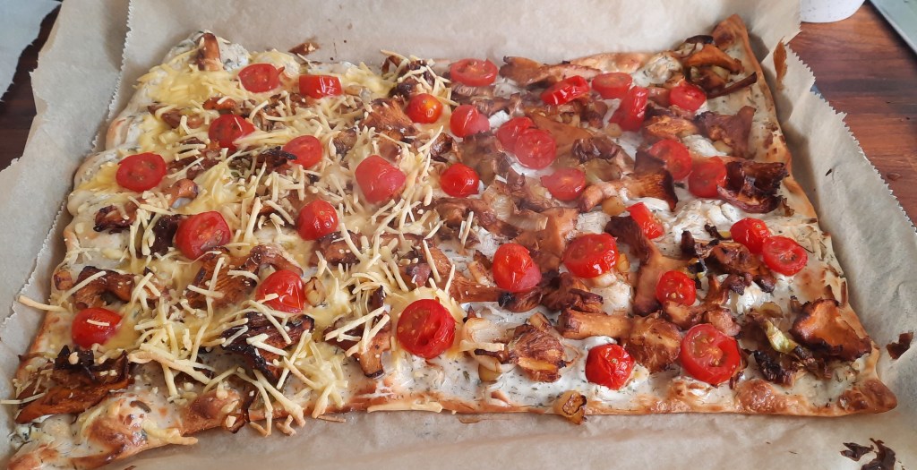 Flammkuchen belegt mit Pfifferlingen, Kirschtomaten, Lauch und auf der linken Seite mit Käse