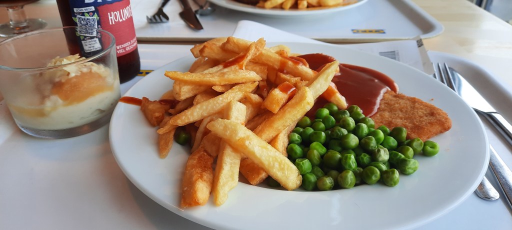 Ein Teller mit Pommes, Erbsen und einem pflanzlichen Schnitzel. Auf dem Schnitzel ist Curry Ketchup.