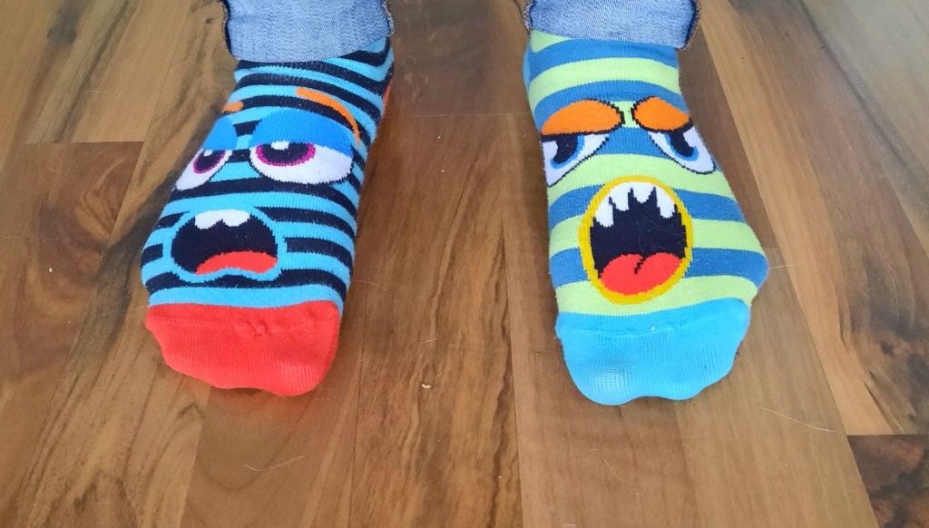 Zwei Füße, an denen unterschiedlich farbende Socken zu sehen sind