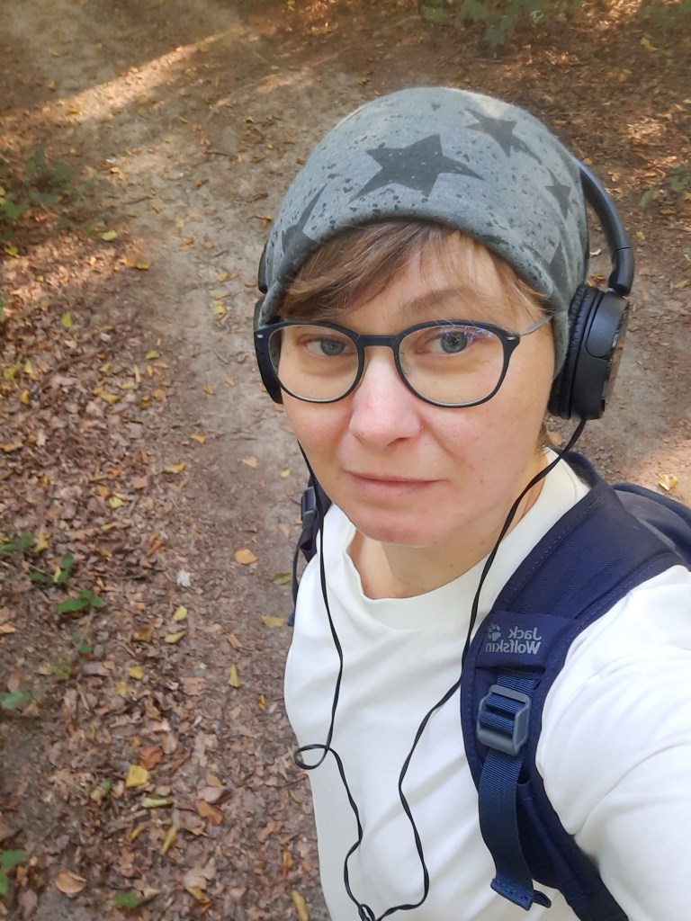 Frau mit grauer Mütze und Kopfhörern im Wald