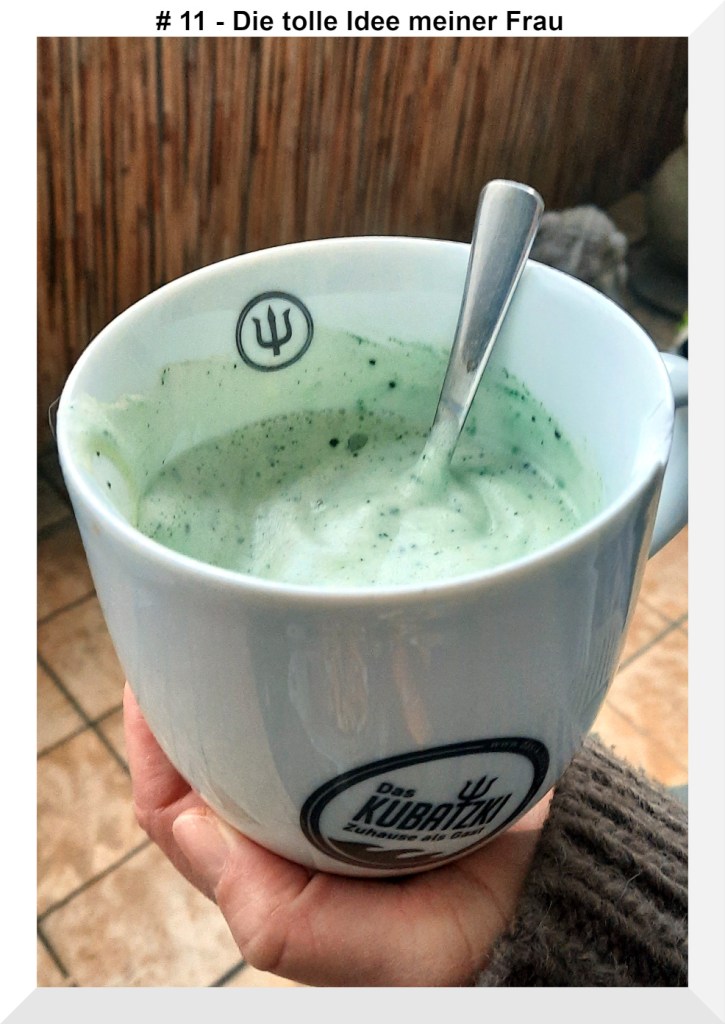 Eine Tasse Kaffee mit Milchschaum und in dem Milchschaum sieht man die grünen Spirulina Krümmel 