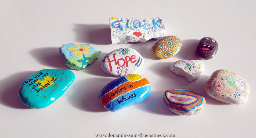 10 bunt bemalte Steine auf weißem Untergrund