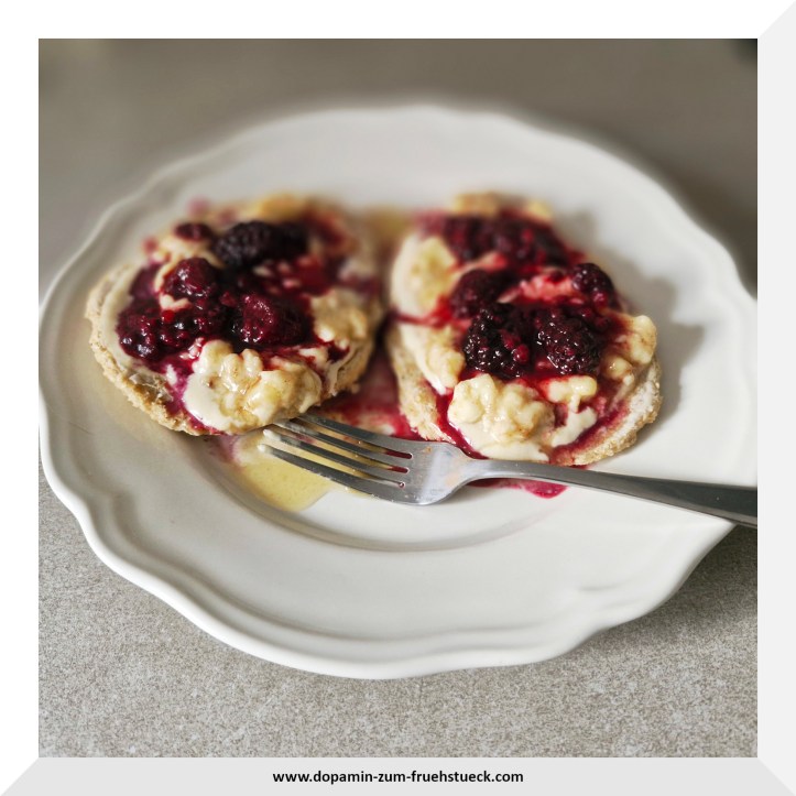 Ein Teller auf dem zwei Haferflockenpfannenbrote liegen. Auf den Broten sind zermatschte Bananen, Beeren und Ahornsirup