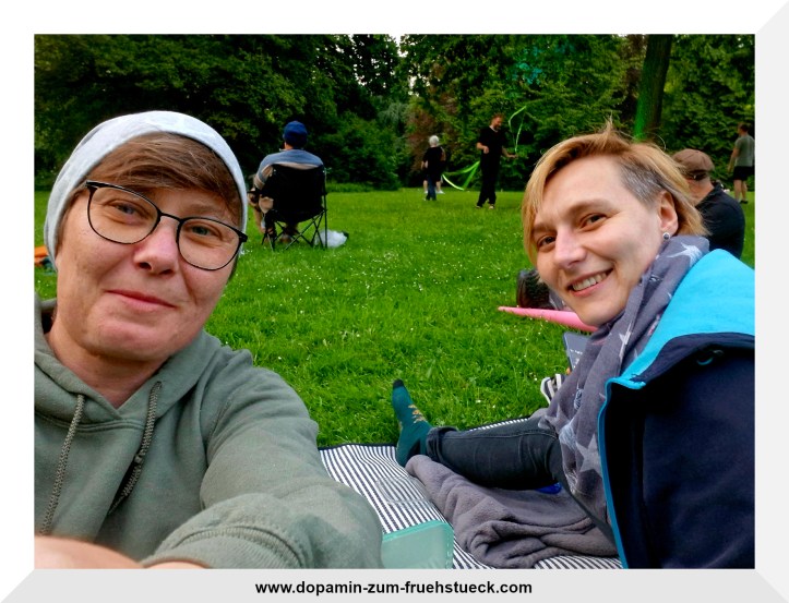 Zwei Frauen, die auf einer Wiese sitzen und in die Kamera lächeln