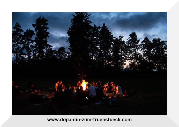 Menschen, die in angehender Dunkelheit vor einem Lagerfeuer sitzen